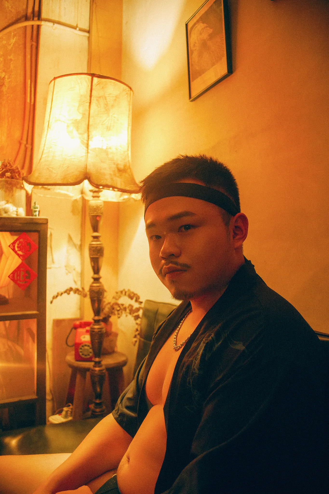 男子坐在昏黃燈光的房間角落，帶著沉思的神情 | 男性寫真攝影 | 宇宙拿鐵