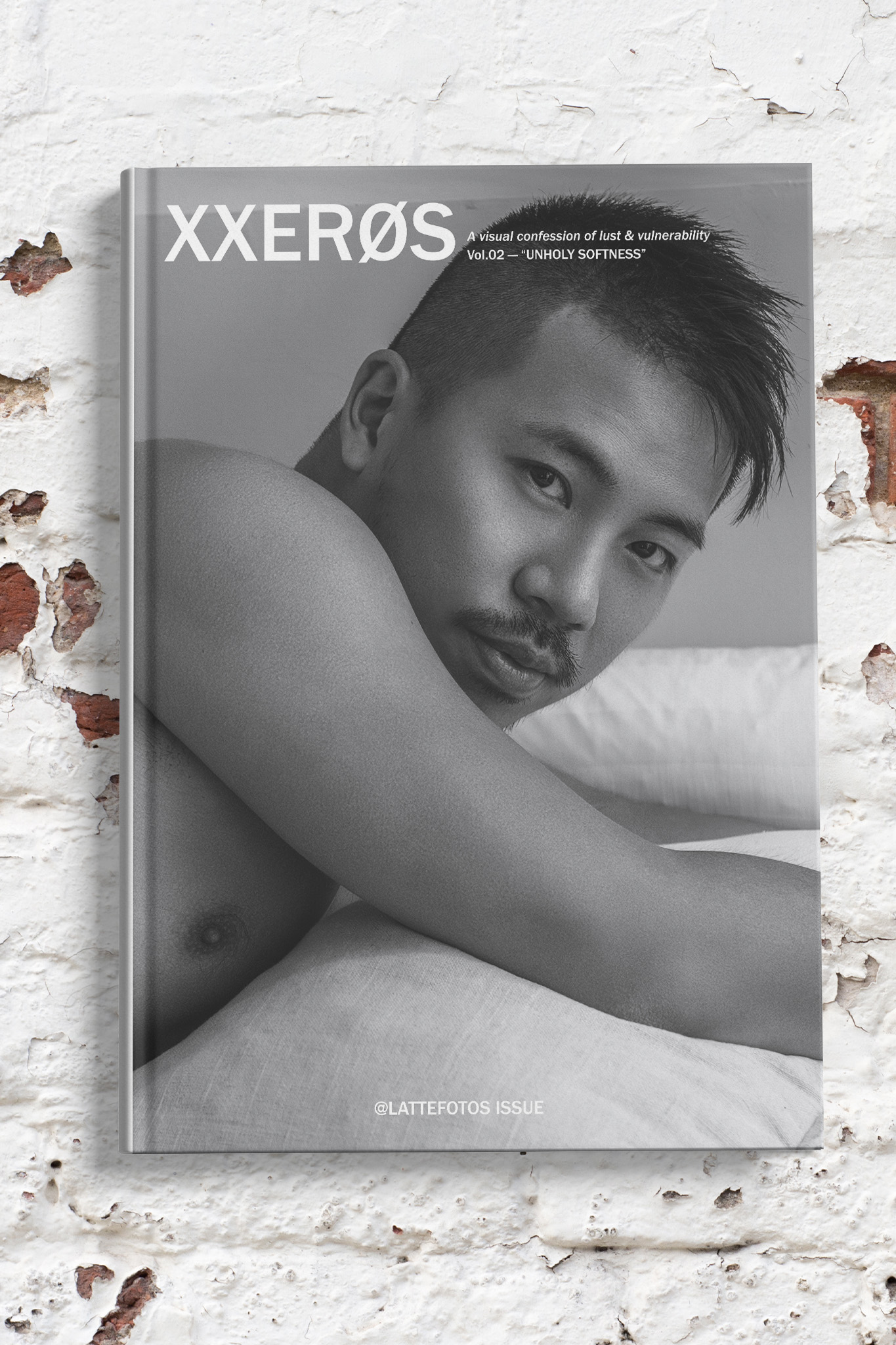 男體寫真誌封面：黑白影像中男子側臥床上，手臂交疊環抱膝蓋，眼神直視鏡頭